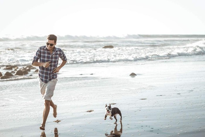 man running on the beach with his dog